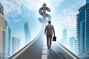 A businessman walking on a road toward a large dollar sign in the sky