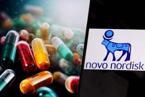 A smartphone showing the logo for Novo Nordisk next to a pile of pills
