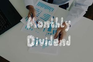 The words “monthly dividend” in front of an investor or businessman holding papers at a desk