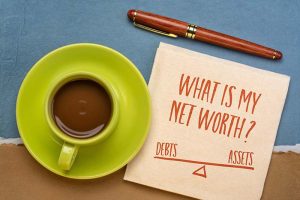 A sticky note reading “What is my net worth?” with “debts” and “assets” on a see-saw