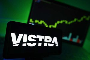 The Vistra logo on a smartphone with a stock chart in the background