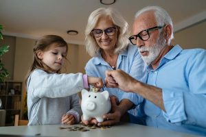 A pair of grandparents putting coins into a piggy bank with their granddaughter