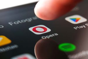 A finger hovering over the Opera app icon on a smartphone screen
