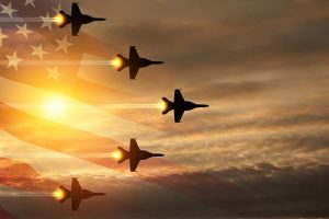 Five U.S. fighter jets at sunset with an American flag superimposed in the background