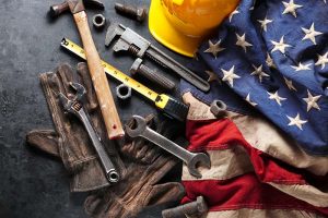 An American flag next to a pile of hammers, wrenches, and other tools
