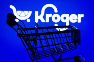 The Kroger logo on a blue backdrop with a shopping cart in the foreground