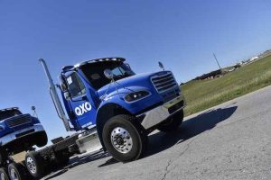 A blue QXO 18-wheeler towing another truck on the highway