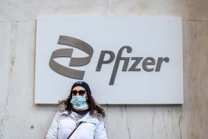 A woman wearing a mask while standing in front of a Pfizer sign