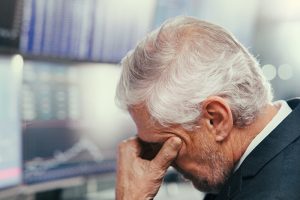 A middle-aged man sitting at a desk with his hand over his face in distress